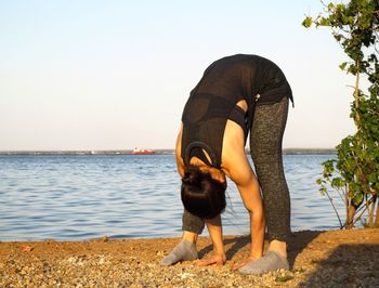 Full length of woman exercising on beach against clear sky