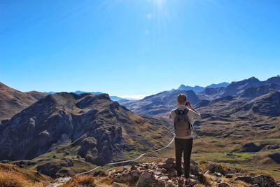 Rear view of boy photographing mountains against clear blue sky