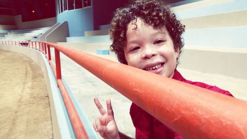 Portrait of cute boy gesturing peace sign by railing at stadium