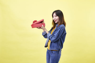 Portrait of smiling young woman standing against yellow background