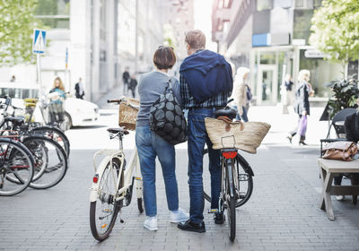 Rear view of senior couple standing with bicycles on city street