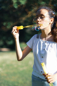 Portrait of a caucasian teenage girl blowing soap bubbles in the park.