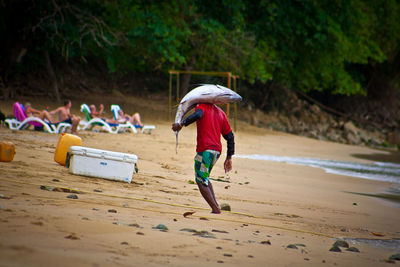 Rear view full length of fisherman carrying fish at beach