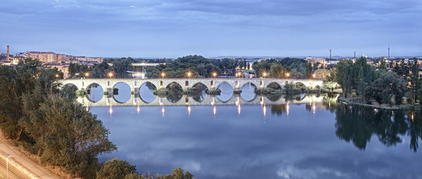 Reflection of illumintaed bridge in water against sky