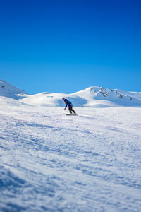 Woman skiing on snowcapped mountain against clear blue sky