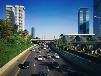 Cars on road by buildings in city against sky