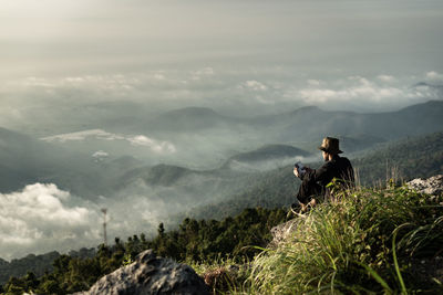Man sitting on mountain against sky