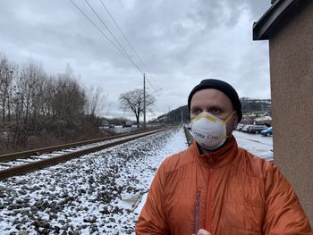 Man wearing mask standing at railroad station during winter