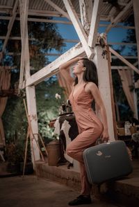 Side view of female model holding suitcase while standing in built structure