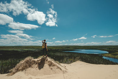 Rear view of woman standing on sand dune against sky during sunny day