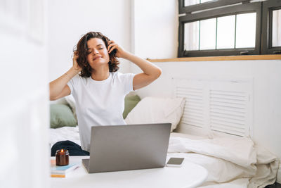 Young woman using laptop while sitting on bed at home