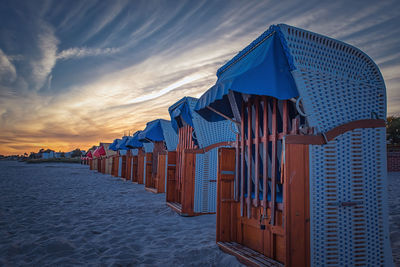 Hooded beach chairs against sky during sunset