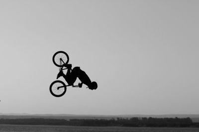 Man with bicycle jumping over sea against clear sky