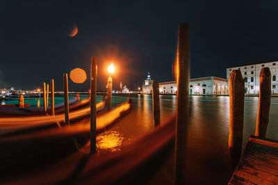 Illuminated street lights by river in city at night