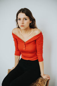 Portrait of a young woman sitting against wall
