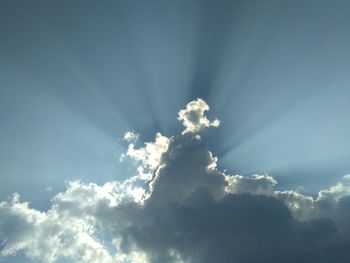 Low angle view of sunlight streaming through clouds