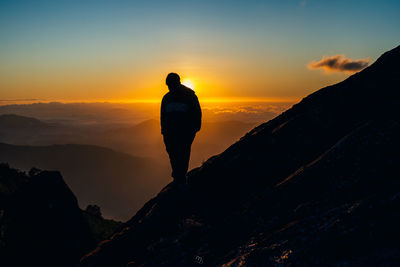 Rear view of silhouette man standing on mountain against sky during sunset