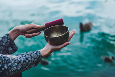 Cropped image of hand holding rin gong over lake