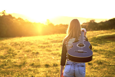 Rear view of woman carrying guitar on field