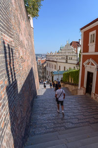 Rear view of women walking on footpath amidst buildings in city