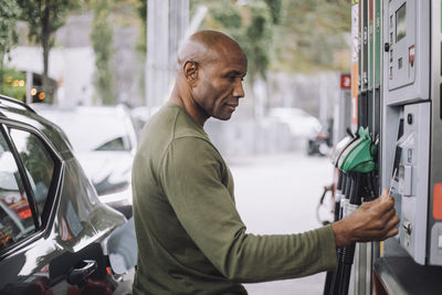 Side view of mature man doing payment through credit card while standing at gas station