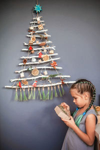 Girl holding gift against christmas tree hanging on wall