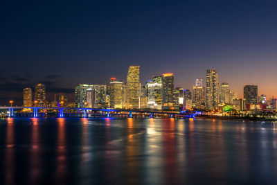 Illuminated buildings by river against sky at night