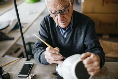 Senior man decorating ceramic vase in his spare time