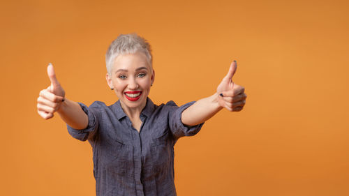 Portrait of happy woman showing thumbs ups against orange background