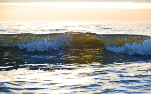 Wave splashing in sea against sky during sunset