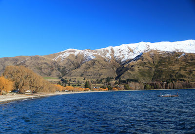 Scenic view of lake and mountains against clear blue sky