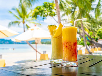 Yellow drink in glasses on table against swimming pool