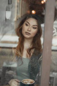 Thoughtful beautiful woman sitting at cafe seen through glass