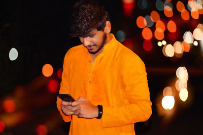 Young man using mobile phone while standing outdoors at night