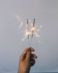 Cropped hand of woman holding sparklers against sky