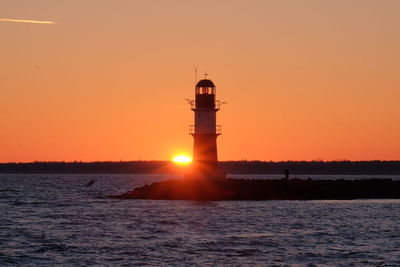 Lighthouse by sea against sky during sunset