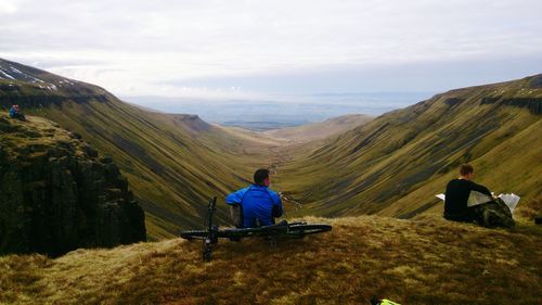 Rear view of men sitting on mountain against sky