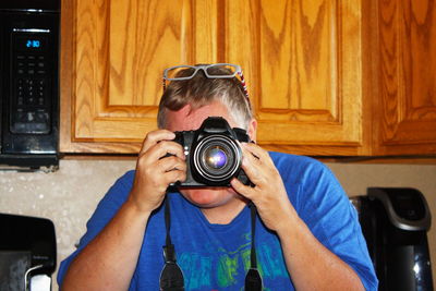 Man photographing through camera while sitting at kitchen