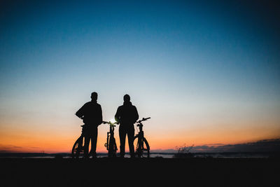 Silhouette people riding bicycle against clear sky during sunset