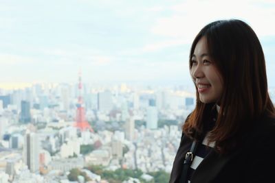 Portrait of smiling young woman standing against cityscape