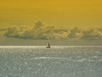 Mid distant view of sailboat sailing on seascape against sky during sunset