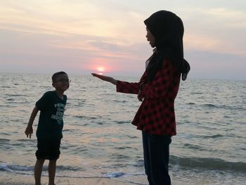 Woman standing on beach against sky during sunset