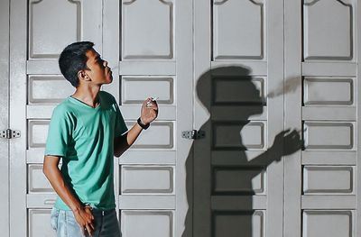 Man smoking cigarette while standing against doors