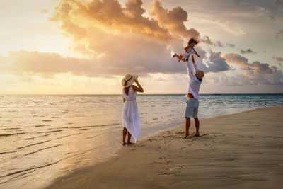 Cheerful father tossing daughter mid air while standing at beach during sunset