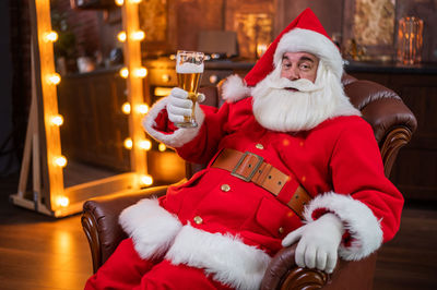 Portrait of santa clause holding beer sitting at home