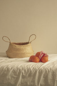 Wicker basket with oranges on bed against wall at home