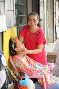 Portrait of smiling woman massaging face while sitting outdoors