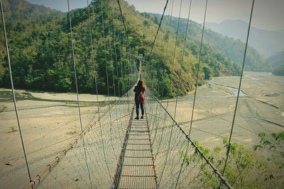 Rear view of woman standing on rope bridge