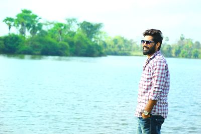 Smiling man standing by lake against sky