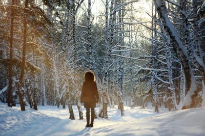 Rear view of woman walking in snow covered forest